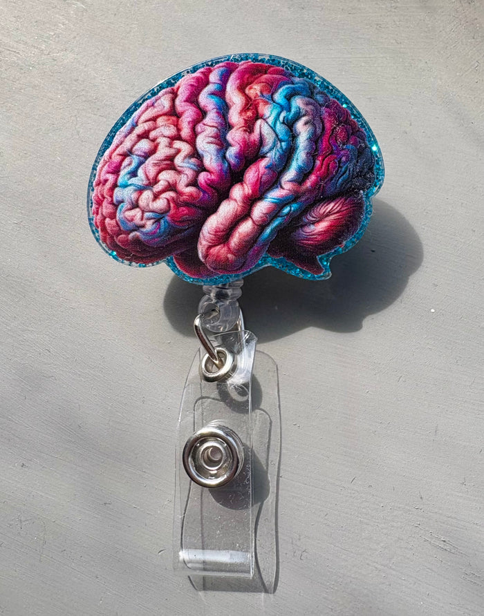 Colorful anatomical brain badge reel with pink and blue design on glittery blue background and retractable clip for medical ID or name badge.
