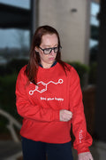 Dr. Betsy Grunch - Ladyspinedoc - wearing a red dopamine molecule sweatshirt and showing off the heart of medicine logo printed on the inner left sleeve, symbolizing the heartbeat of patient care.