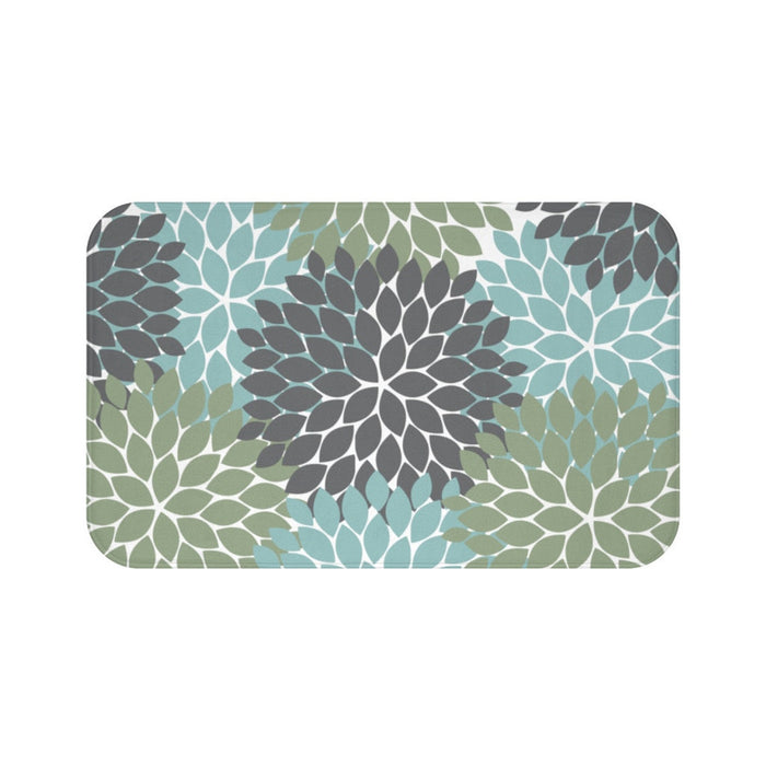 A rectangular memory foam mat with a sage green, gray, and blue floral pattern and anti-slip backing.