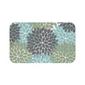 A rectangular memory foam mat with a sage green, gray, and blue floral pattern and anti-slip backing.