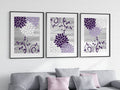 A set of three purple and gray floral wall art prints arranged vertically on a wall above a gray sofa with pink and gray cushions.